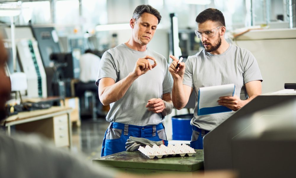 Industrial workers cooperating while doing quality control of manufactured products in a factory.